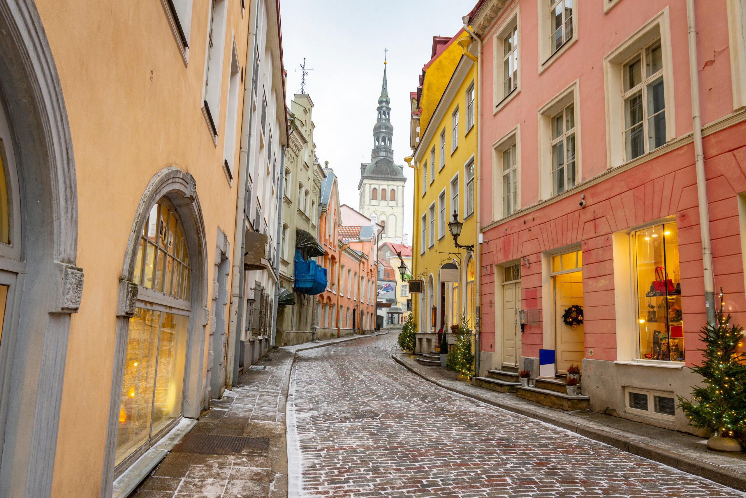 A narrow street in old town on a cold winter day in Estonia. It shows colourful houses and a church in the background.